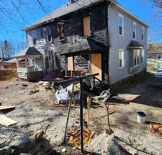 Residential building with fire damage, featuring boarded windows and charred exterior.