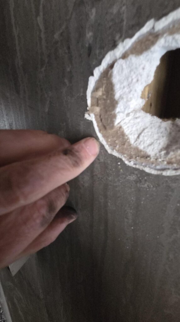 A hand points to a damaged wall opening with torn plaster and exposed inner material